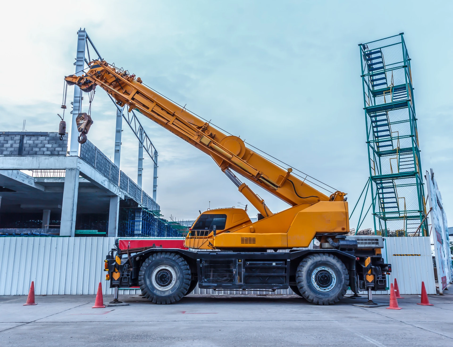 Chantier de construction extérieur avec grue mobile orange stationnée près d'un bâtiment en béton en cours d'édification