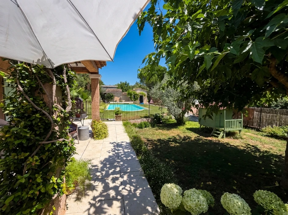 Jardin privatif ensoleillé avec piscine rectangulaire clôturée en fer forgé noir, terrasse en carrelage grès cérame beige, pergola avec voile d'ombrage blanc
