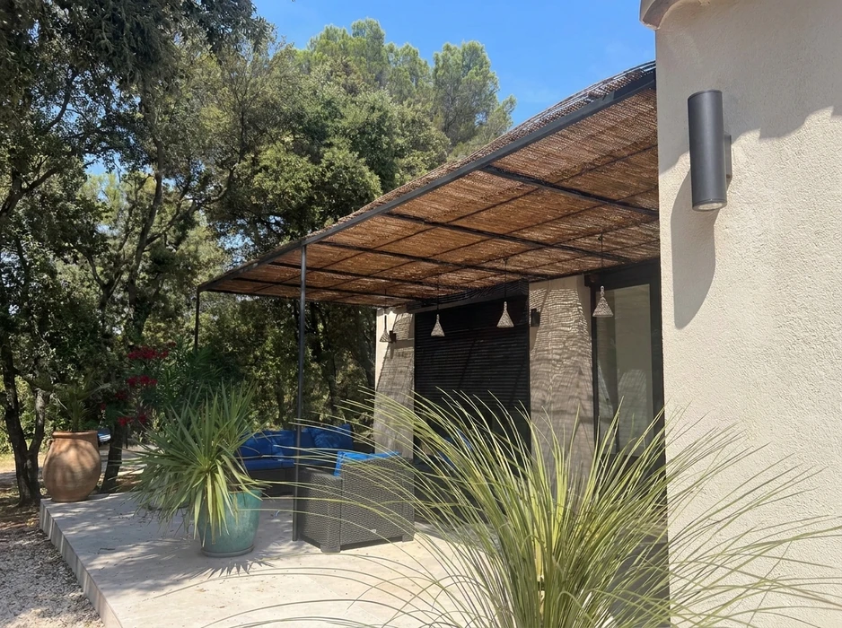 Terrasse extérieure moderne avec pergola en acier noir supportant un toit en canisse