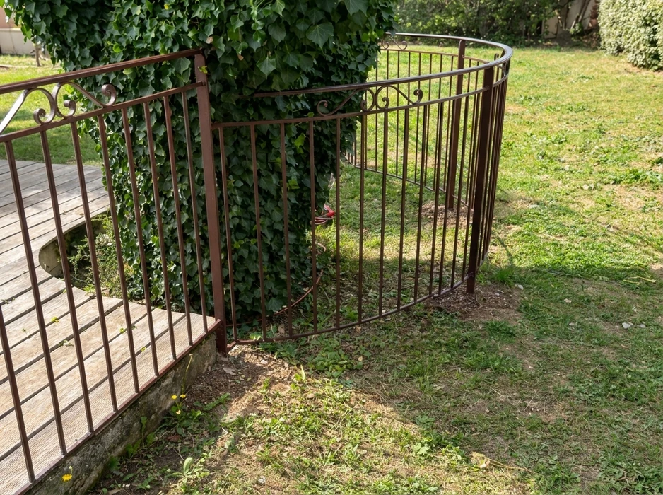 Jardin extérieur ensoleillé avec une clôture en fer forgé marron rustique à barreaux verticaux, ornée de volutes décoratives en partie supérieure