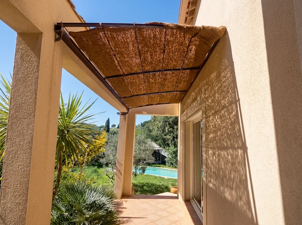 Terrasse couverte d'une villa méditerranéenne, vue sur piscine et jardin arboré