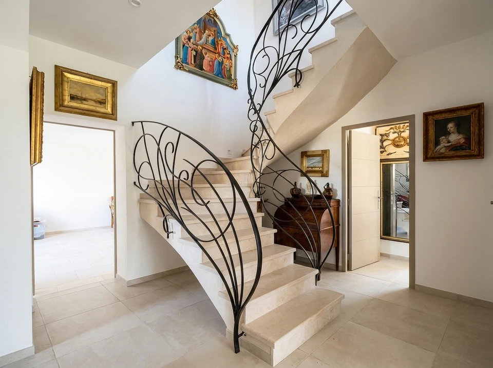 Entrée de villa luxueuse avec escalier en pierre calcaire beige à balustrade en fer forgé noir aux volutes végétales