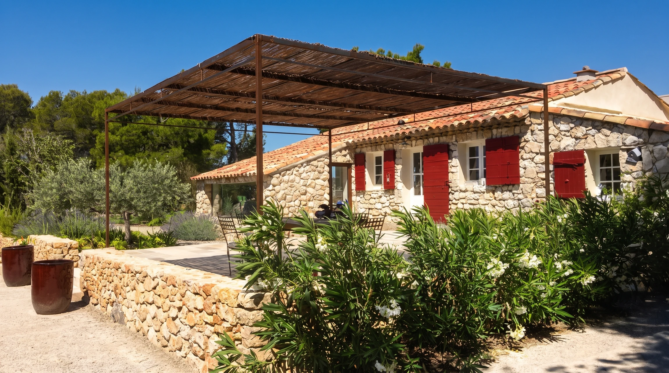 Mas provençal en pierres sèches avec volets rouges et toiture en tuiles canal, entouré d'oliviers et d'oléandres