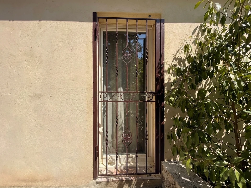 Entrée majestueuse d'une propriété provençale, portail en fer forgé patiné entre deux piliers en pierre calcaire taillée, flanqués d'un muret en pierres sèches